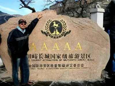 The writer standing next to the stone nameplate for the Mutianyu Great Wall. The stone monument identifies the site as a National Tourist Attraction of Mutianyu Great Wall, officially designated as a AAAAA (5A) scenic area— the highest rating for tourist attractions in China.
