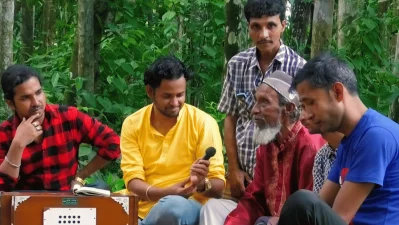 Sitting along with two of his sons near his home, Khuaj Mia talking to a YouTube channel. Photo: Dhaka Tribune/Collected