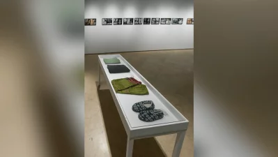A glass display vitrine containing personal artifacts belonging to Novera Ahmed, showcased as part of the biographical section of her retrospective exhibition. These include carefully folded garments—such as a traditional green-and-red patterned saree—and a pair of well-worn, patterned fabric indoor slippers. Photo: Collected/Dhaka Tribune