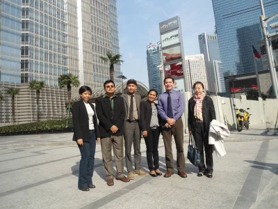 Visitors posing together outside the Jin Mao Tower plaza area in the Lujiazui financial district of Pudong, Shanghai. The tall totem sign in the center background reads J·LIFE, a high-end retail, dining, and lifestyle center located inside the podium of the Jin Mao Tower.