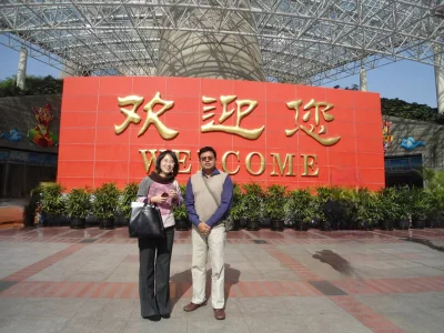 The writer along with a local host standing in front of the primary entrance plaza of the Oriental Pearl Tower in Shanghai, China. Behind them the distinctive large red greeting wall features the gold lettering “欢迎您” (Huānyíng nín) – Welcome. Located in the Pudong New Area of Shanghai, Oriental Pearl TV Tower stands right at the tip of the Lujiazui peninsula, the prominent financial district on the eastern bank of the Huangpu River.