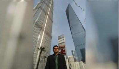 The writer standing in the Lujiazui financial district of Pudong, standing between landmark skyscrapers – 1,380 feet Jin Mao Tower and 1,614 feet Shanghai World Financial Center.