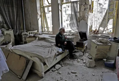 Mohammad Mohiedine Anis, 70, smokes his pipe as he sits in his destroyed bedroom listening to music on his vinyl player, gramophone, in Aleppos formerly rebel-held al-Shaar neighbourhoodrnrnAFP
