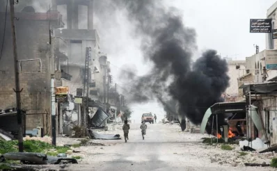 A picture taken on March 22, 2017 in the Syrian town of Tayyibat al-Imam in the countryside of the central province of Aleppo, shows fighters running amdist destruction down a street past a rising plume of smoke from a burning tire meant to disrupt warplanesrnrnAFP