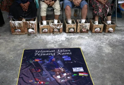 In this Wednesday, March 22, 2017 photo, a poster of Patmi binti Rustam who died while taking part in the protest against the operation of a cement factory in Kendeng, Central Java, is displayed as activists have their feet encased in concrete during a rally outside the presidential palace in Jakarta, Indonesia. Dozens of farmers and activist have battled against the operation of a cement factory in Kendeng, Central Java for years, saying it could taint their water. The protest was overshadowed by the death of Patmi early TuesdayrnrnAP