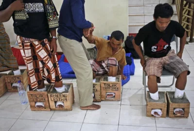In this March 19, 2017 photo, a protester whose feet are encased in concrete is assisted to stand up at their temporary shelter at the Legal Aid Institute office in Jakarta, IndonesiarnrnAP