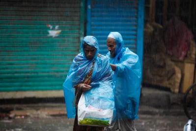 A man helps a woman with a plastic drape to avoid getting drenched in the rain | Mahmud Hossain Opu