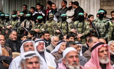Palestinian men watch as fighters from the Ezzedine al-Qassam Brigades, the armed wing of the Palestinian Hamas movement, take part in a military show ahead of the 30th anniversary of the movements founding in the southern Gaza Strip city of Khan Yunis on December 5, 2017 (AFP)