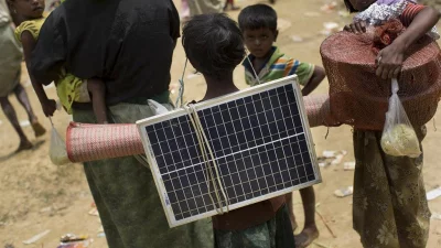 In this Thursday, September 7, 2017, photo, a Rohingya Muslim child carries a solar panel as she crosses over the border from Myanmar into Bangladesh in Teknaf area AP