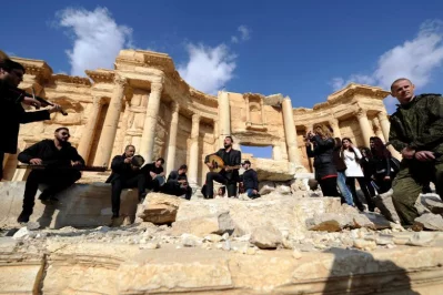 A Russian soldier stands near Syrian musicians as they play their instruments while resting on damage in the amphitheater of the historic city of Palmyra, SyriarnrnREUTERS