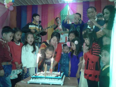Children gather around a cake being cut while musicians create a festive mood at the backdrop in Khagrachari | Nuruchsafa Manik/Dhaka Tribune