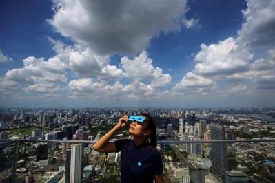 A woman observes a partial solar eclipse on the Mahanakhon Skywalk Glass Tray at the King Power Mahanakhon building in Bangkok, Thailand, June 21, 2020 Reuters