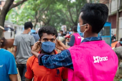 A BRAC volunteer, demonstrating the proper way of wearing a mask to an individual in a marketn