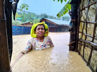 An elderly woman stands under the rain by the door of her flooded shelter. In 2021, the Rohingya refugee camp was hit by massive floods affecting thousands of refugees, mostly vulnerable women and children Shahida Win 2021