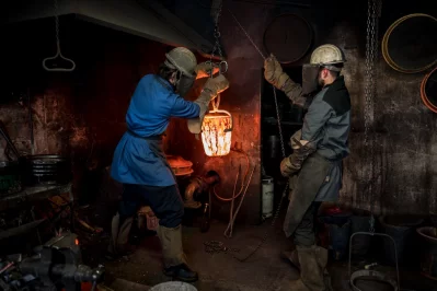 Alois Huguenin and an assistant move a ladle of molten bronze in his foundry