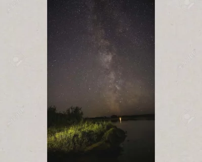 The Milky Way is vividly visible in the night sky with its dense core and dust lanes of our galaxy in this amazing shot captured from the dark shoreline of South Saskatchewan River with illuminated grass at Cranberry Flats.