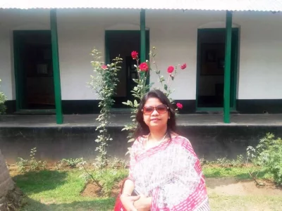 A visitor at the courtyard of Kachari Bari, characterized by its white walls, dark base, and distinctive green pillars and door frames, as seen in the background. Photo: Dhaka Tribune/Collected