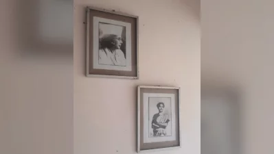 Two framed photographs on the wall &ndash; top left one shows a profile view of Nazrul in his later years wearing his iconic cap and glasses while the bottom right portrait depicts youthful poet with his arms crossed, wearing a traditional shawl. This image is widely associated with his legendary revolutionary poem, Bidrohi (The Rebel), penned in 1921