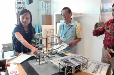The image shows a demonstration of base isolation technology used in earthquake-resistant building design. Base isolators are special pads or bearings placed between a building and its foundation to absorb and reduce seismic forces by allowing the ground to move while the building remains relatively steady.
