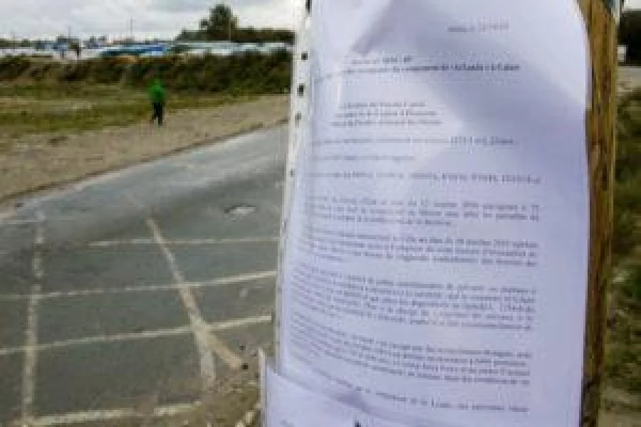 A man walks by a pillar where is displayed the advice notice for evacuation concerning the "jungle" migrant makeshift camp in Calais, on October 21, 2016. The "Jungle" migrant camp on France's northern coast will be cleared of its residents on October 24, 2016 before being demolished, authorities said on October 21. Migrants at the camp in the ferry port of Calais will begin boarding 145 buses at 8:00 am (0600 GMT) on October 24 to take them to nearly 300 temporary accommodation centres dotted round France. The demolition of the sprawling makeshift camp closes a difficult chapter in Europe's migrant crisis. / AFP PHOTO / DENIS CHARLET