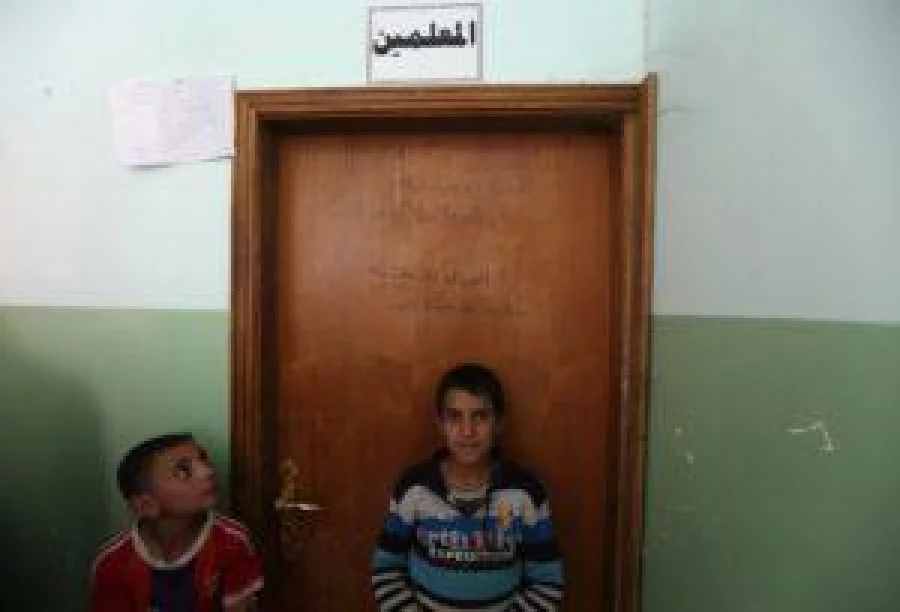 Iraqi boys stand under a slogan written on a door inside their school by members of the Islamic State group in Jarif, some 45 kilometres south of Mosul, on November 12, 2016, after Iraqi forces retook the village from IS jihadists. / AFP PHOTO / SAFIN HAMED