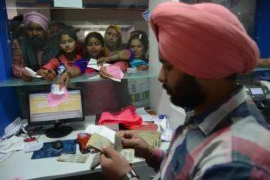 An Indian bank teller counts out notes as people gather inside a bank to deposit and exchange 500 and 1000 rupee notes in Amritsar on November 15, 2016. Long queues formed outside banks in India since the government's shock decision to withdraw the two largest denomination notes from circulation.  / AFP PHOTO / NARINDER NANU