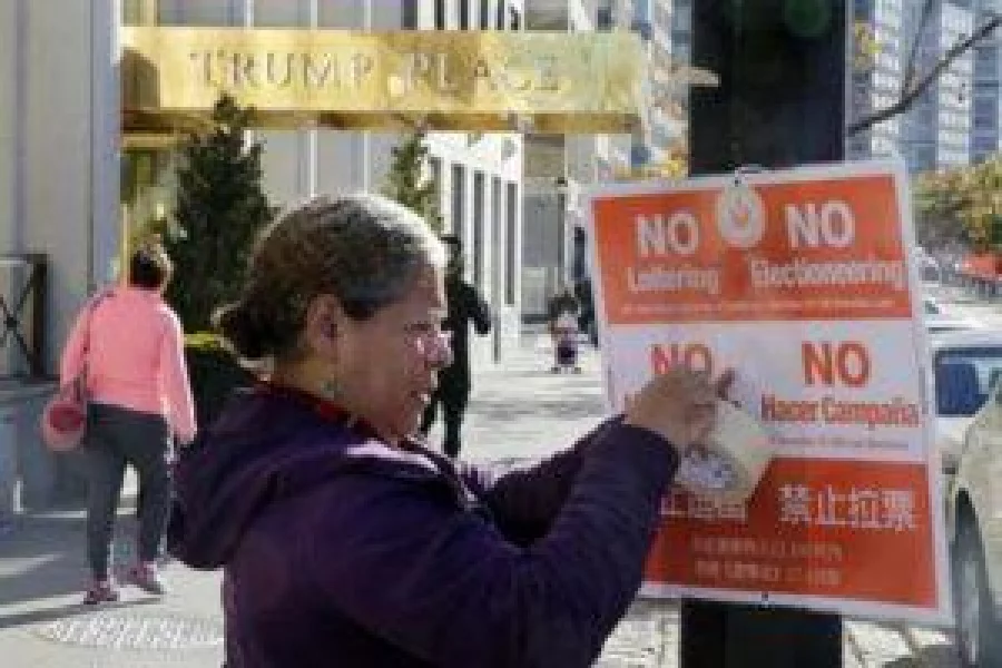 In this Nov. 8, 2016 file photo, poll interpreter Mayra Mora affixes a sign outside of a polling place in an apartment building named for then Republican presidential candidate Donald Trump, in New York. The luxury apartment building is one of three that will have the president-elect's name stripped from it after hundreds of residents signed an online petition demanding it be removed. (AP Photo/Richard Drew, File)
