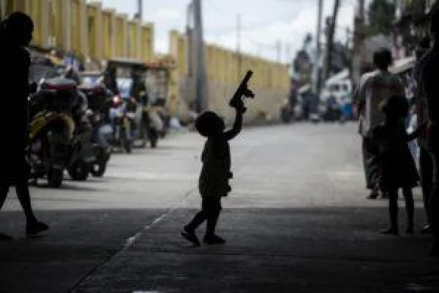A child is silhouetted while playing with a toy gun as police officers conduct a "Oplan Tokhang" or a house-to-house campaign on illegal drugs at an informal settlers community in Manila on October 6, 2016.  Philippine President Rodrigo Duterte told all his critics to "go to hell" on October 6, as he renewed his threats to kill, after a poll showed Filipinos overwhelmingly endorsed his deadly war on crime.  / AFP PHOTO / NOEL CELIS