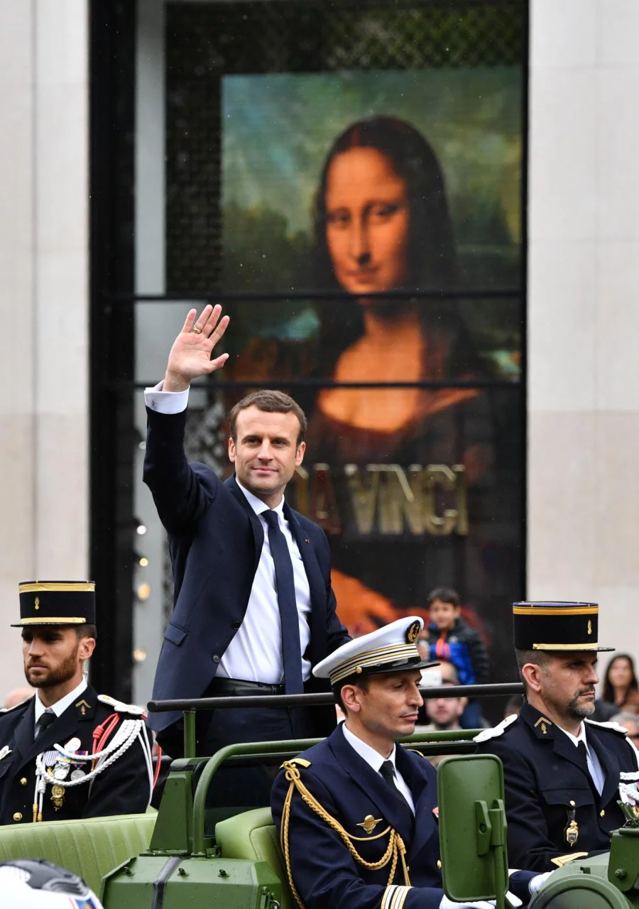 French President Emmanuel Macron waves next to a replica of the painting Mona Lisa by Leonardo da Vinci, displayed on the shop window of a Louis Vuitton store, as he parades in a car on the Champs Elysees avenue after his formal inauguration ceremony as French President on May 14, 2017 in Paris. / AFP PHOTO / Mladen ANTONOV