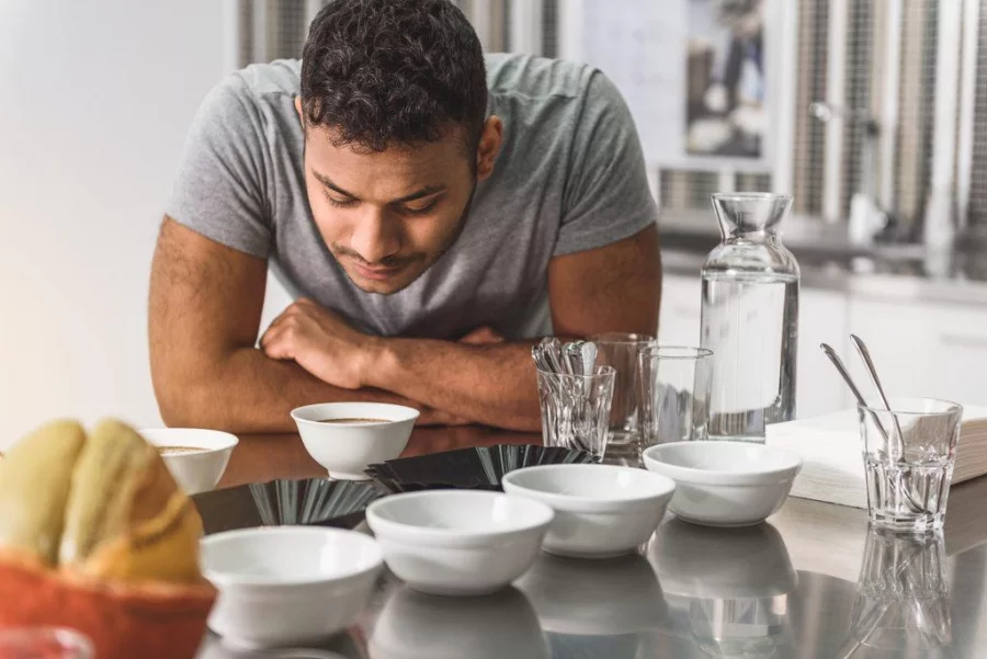 Concentrated male person is standing nearby table. He smelling aroma of coffee