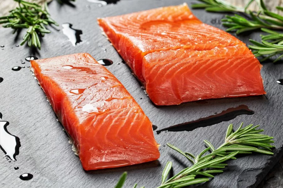 salmon fillet with fresh rosemary and drops of olive oil on slate plate on old dark wooden table close-up