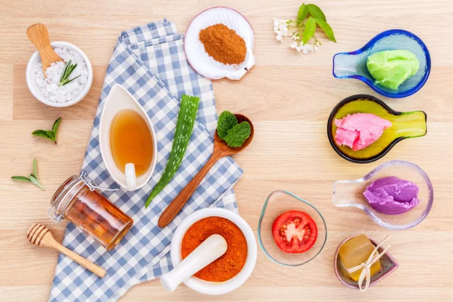 Alternative skin care and homemade scrubs with natural ingredients sage turmeric sea salt honey aloe vera rosemary mint and tomato setup on wooden table.