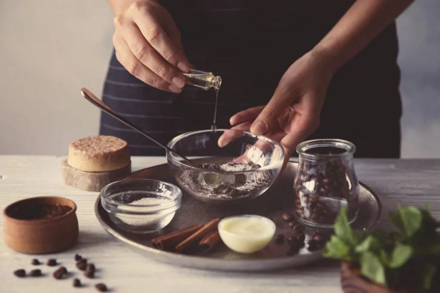 Woman making coffee body scrub on wooden table