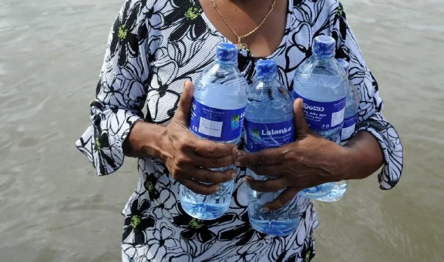 A Sri Lankan woman carries bottles of water through floodwaters in Dodangoda village in Kalutara on May 28, 2017. Emergency teams rushed to distribute aid on May 28 to half a million Sri Lankans displaced after the island's worst flooding in more than a decade claimed 126 lives and left scores more missing.  / AFP PHOTO / Lakruwan WANNIARACHCHI